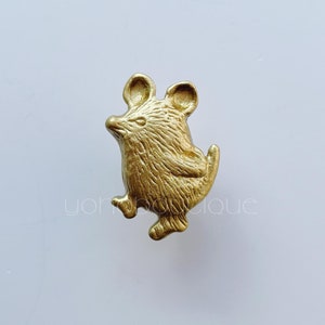 May include: A gold-colored mouse figurine with a textured surface. The mouse is depicted in a walking pose, with its ears and tail visible. The figurine is likely a decorative item or a small sculpture.