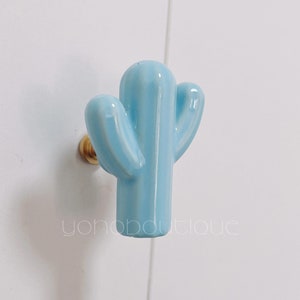Può includere: Un pomello per armadio in ceramica blu chiaro a forma di cactus con una vite dorata.