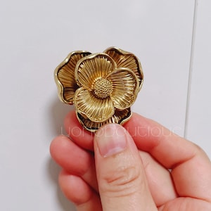 Könnte beinhalten: Ein goldfarbenes, metallisches Dekorationsstück in Form einer Blume mit einer strukturierten Oberfläche.