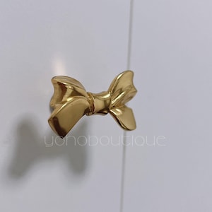 Puede incluir: Pomo de armario dorado en forma de lazo.