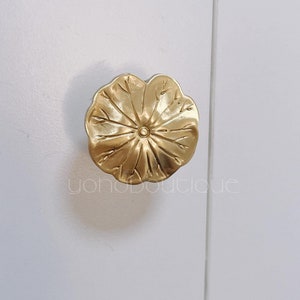 Könnte beinhalten: Goldfarbener, blumenförmiger Schrankknopf mit detailliertem Design.