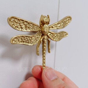 May include: Gold-toned dragonfly door knob with intricate details. The dragonfly is mounted on a white wall.