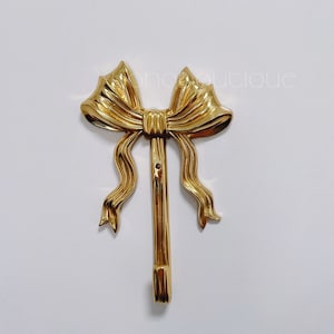 Peut inclure: Un crochet en métal doré en forme de nœud. Le crochet est conçu pour accrocher des objets au mur.