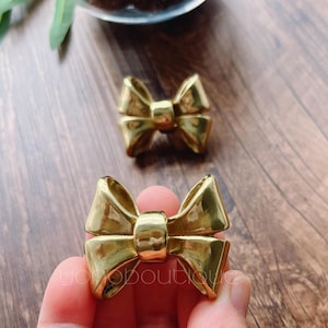 Peut inclure: Deux pièces décoratives en métal en forme de nœud de couleur or. Les nœuds mesurent environ 5 cm de long et 2,5 cm de large.