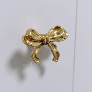 May include: Gold bow-shaped cabinet knob with a detailed design.
