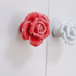 May include: Two ceramic rose-shaped drawer pulls. One is pink and the other is white.