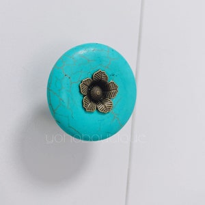 Może przedstawiać: Gałka meblowa w kolorze turkusowym z złotym wzorem kwiatu.