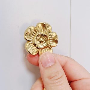 Pode incluir: Uma maçaneta de armário de metal dourado em forma de flor com um centro elevado.