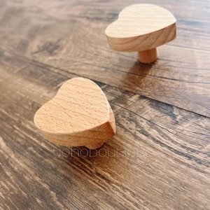 Può includere: Due pomelli di legno a forma di cuore, uno sopra l'altro, su una superficie di legno.