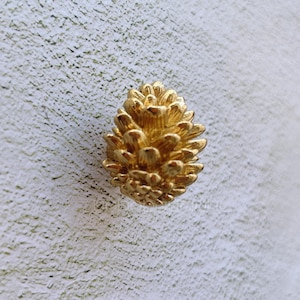 Puede incluir: Un pomo de armario en forma de piña de color dorado.