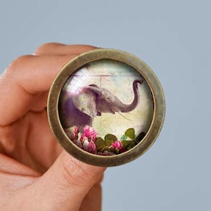 May include: A round, brass-colored pendant with a glass dome featuring a vintage image of an elephant with its trunk raised, surrounded by pink flowers.