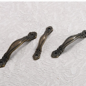 May include: Three antique bronze cabinet handles with ornate floral detailing. The handles have a curved design and are approximately 5 inches long, perfect for adding a vintage touch to furniture.