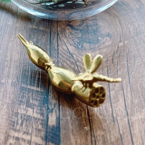 Puede incluir: Una figurita de libélula de metal dorado con detalles intrincados. La libélula está posada sobre una superficie de madera.