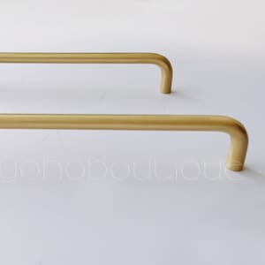 Pode incluir: Dois puxadores de armário de metal dourado com forma retangular arredondada. Os puxadores medem aproximadamente 12,5 cm de comprimento.