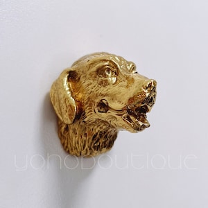 Könnte beinhalten: Eine goldfarbene Metallskulptur eines Hundekopfes. Der Hund hat den Mund offen und die Zunge hängt heraus. Die Skulptur ist detailliert und realistisch.