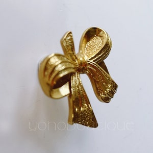May include: A gold-toned metal bow-shaped door knob or drawer pull.