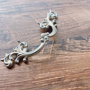 以下が含まれることがあります： 装飾的なスクロールデザインが施された銀色の装飾的な引き出しノブです。