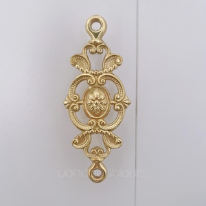 May include: Gold metal decorative wall hook with a floral design. The hook has two rings at the top and bottom.