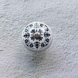 Pode incluir: Botão de cerâmica branco com um design floral preto e branco. O botão tem um centro de metal prateado.