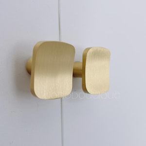 Op de afbeelding: Twee gouden vierkante kastknoppen met een geborstelde afwerking.