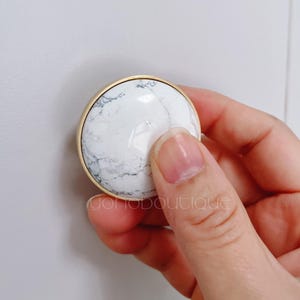 May include: A round cabinet knob made of white marble and gold.