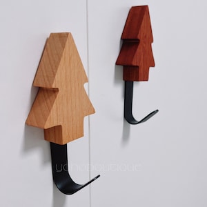 May include: Two wooden tree-shaped hooks with black metal hooks. The hooks are mounted on a white wall.