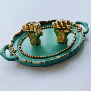 Pode incluir: Uma bandeja decorativa verde e dourada com duas alças douradas em forma de punho. A bandeja é oval e tem uma borda com contas.