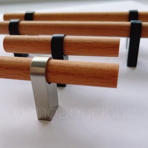 Puede incluir: Cuatro pomos de armario de madera con detalles metálicos negros y plateados. Los pomos están dispuestos en fila, con el pomo plateado en la parte inferior.