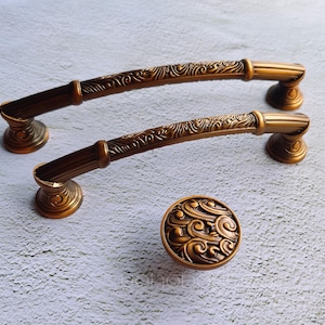 Può includere: Due maniglie per ante di armadio ornate in color oro con un motivo floreale decorativo. È incluso anche un pomo dorato abbinato con un motivo floreale simile.