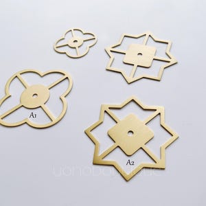 May include: Four brass decorative hardware pieces with geometric designs. Two pieces are shaped like a four-leaf clover with a hole in the center. The other two pieces are shaped like a star with a hole in the center. The pieces are labeled A1 and A2.