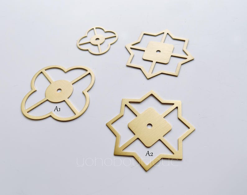 May include: Four brass decorative hardware pieces with geometric designs. Two pieces are shaped like a four-leaf clover with a hole in the centre. The other two pieces are shaped like a star with a hole in the centre. The pieces are labelled A1 and A2.