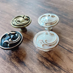 Może przedstawiać: Cztery ozdobne gałki do szafki z kwiatowym wzorem. Gałki są w kolorze złotym, srebrnym, czarnym i białym.