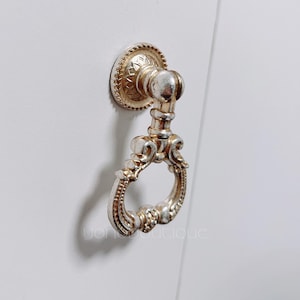 May include: A silver and gold ornate ring pull door handle with a decorative design.