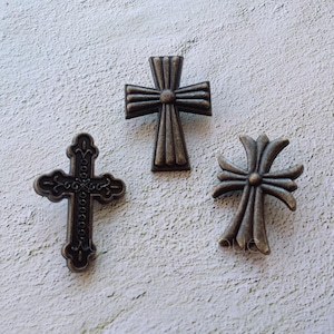 Op de afbeelding: Drie antiek ogende metalen kruisbedels in verschillende stijlen. De kruisen zijn allemaal donkerbrons van kleur en hebben ingewikkelde details.