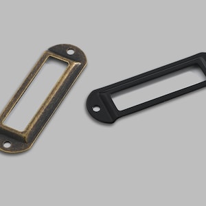 May include: Two metal label holders, one in antique gold and one in black. Both have a rectangular opening for inserting a label.