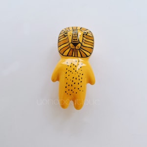 May include: A yellow ceramic figurine of a lion with black details. The lion has a spotted body and a black outlined face with a black nose and eyes.