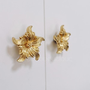 Peut inclure: Deux boutons de porte en forme de fleur dorés. Les boutons ont un design détaillé avec un centre surélevé et des pétales.