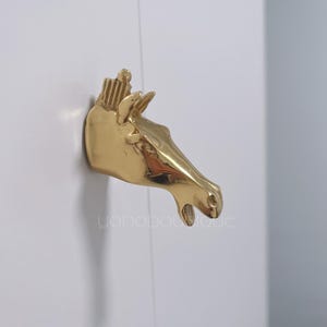 May include: A gold-coloured horse head wall hook. The horse's head is facing to the right and has a detailed design.