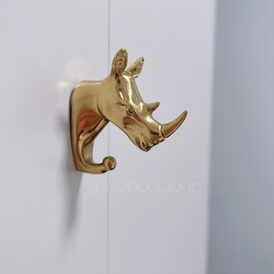 Könnte beinhalten: Ein goldfarbener Wandhaken in Form eines Nashornkopfes. Der Haken ist aus Metall und hat ein realistisches Design.