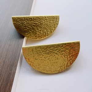 Puede incluir: Dos tiradores de armario de media luna de metal dorado con textura martillada.