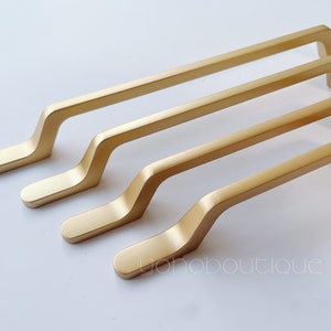 May include: Four gold-colored cabinet pulls with a curved design. The pulls are arranged in a row, with the largest pull at the bottom and the smallest pull at the top.