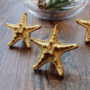 May include: Three gold-toned starfish-shaped drawer pulls. The starfish are textured and have a slightly raised design.