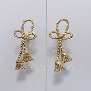 Könnte beinhalten: Ein Paar goldfarbene Ohrringe mit einem seilartigen Design und Quastenakzenten.