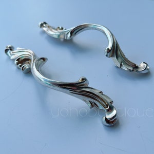 May include: Two silver ornate drawer pulls with a decorative, swirling design.
