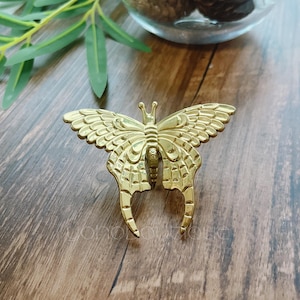 Peut inclure: Une poignée de tiroir en forme de papillon dorée avec des détails complexes. La poignée est en métal et a une finition brillante.