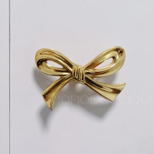 May include: A gold-coloured bow-shaped cabinet knob.