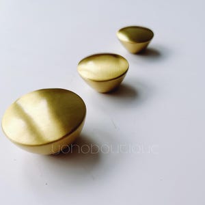 Op de afbeelding: Drie gouden metalen kastknoppen met een afgeronde, licht gewelfde vorm.