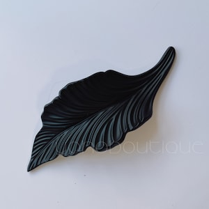 Pode incluir: Uma bandeja de servir preta em forma de folha com um design texturizado. A bandeja é feita de um material durável e é perfeita para servir lanches, aperitivos ou sobremesas.