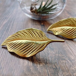 May include: Two gold leaf-shaped decorative drawer pulls with a ribbed texture.