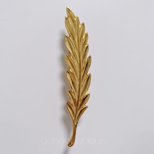 Może przedstawiać: Złoty metalowy akcent dekoracyjny w kształcie liścia. Liść ma szczegółowy, fakturowany wzór.